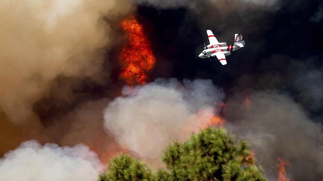 An air tanker flies past flames while battling the Oak Fire in Mariposa County, Calif., Sunday. Wildfires, floods and soaring temperatures have made climate change real to many Americans. Yet a sizeable number continue to dismiss the scientific consensus that human activity is to blame.