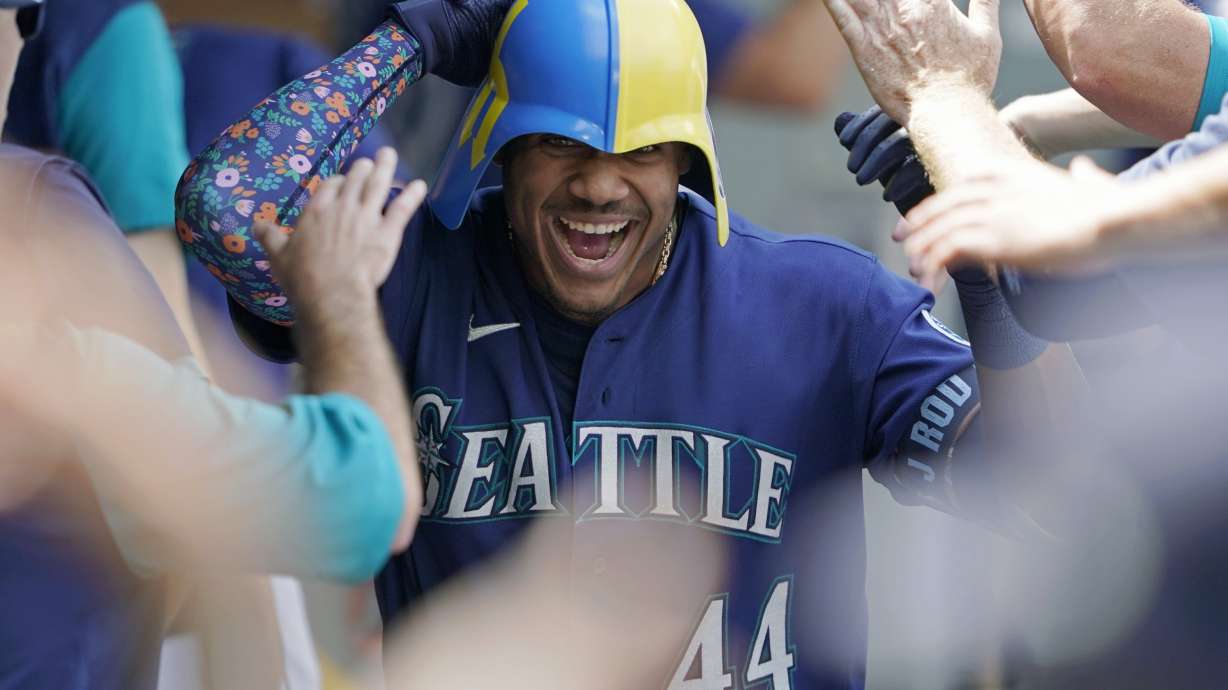 Seattle Mariners' Julio Rodriguez wears a helmet as he is greeted in the dugout after his three-run home run against the Texas Rangers during the seventh inning of a baseball game Wednesday, July 27, 2022, in Seattle.