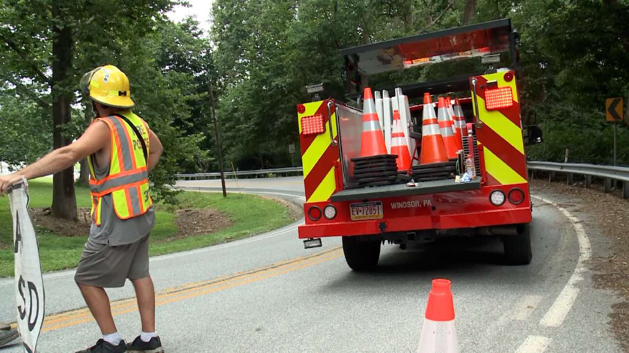A worker monitors a road closure near the scene of an accident. Four people are dead, including three children, after a tractor towing a flatbed-type utility trailer carrying 12 people rolled over Friday morning in southeastern Pennsylvania, state police said.