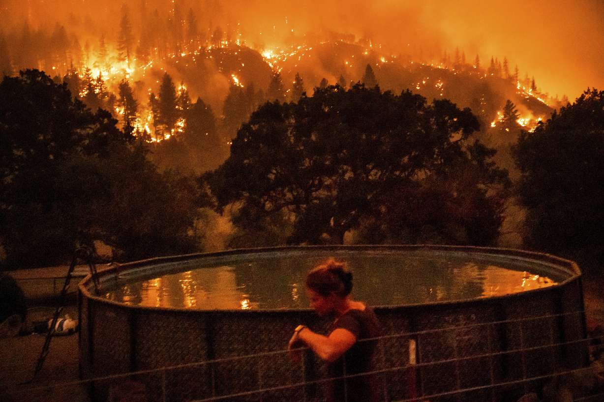 Angela Crawford leans against a fence as a wildfire called the McKinney fire burns a hillside above her home in Klamath National Forest, Calif., on Saturday. Crawford and her husband stayed, as other residents evacuated, to defend their home from the fire.