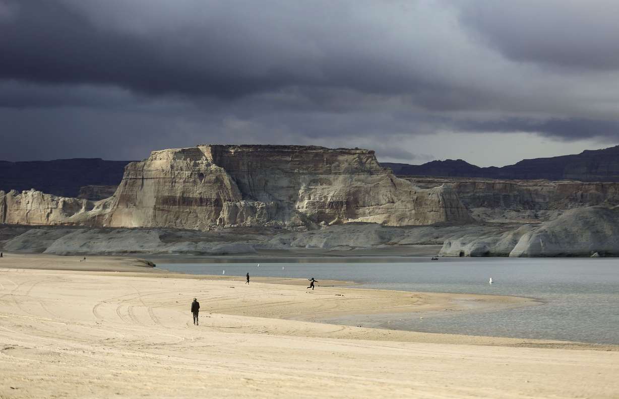People walk at Lone Rock Beach on the shores of Lake Powell in Glen Canyon National Recreation Area in Utah on March 26, 2021.