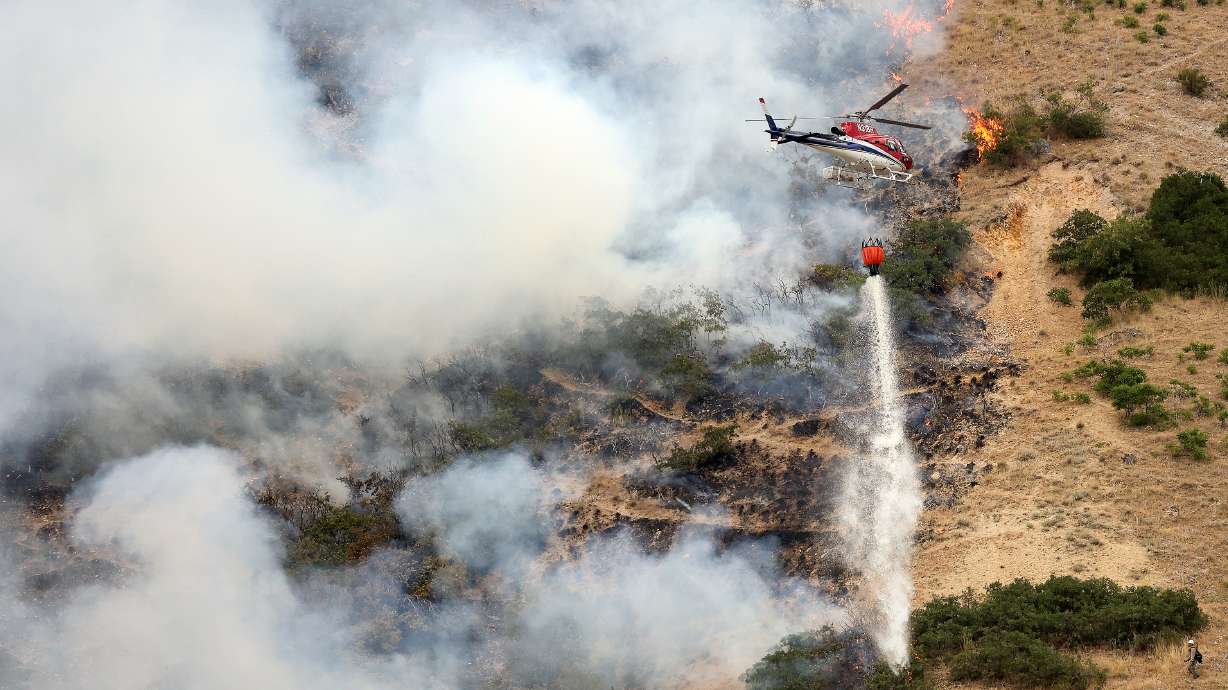 Firefighters battle a wildfire from the ground as a helicopter drops water above them in Springville on Aug. 1, 2022. Utah Gov. Spencer Cox issued an executive order Monday to help the state prepare for the upcoming fire season.