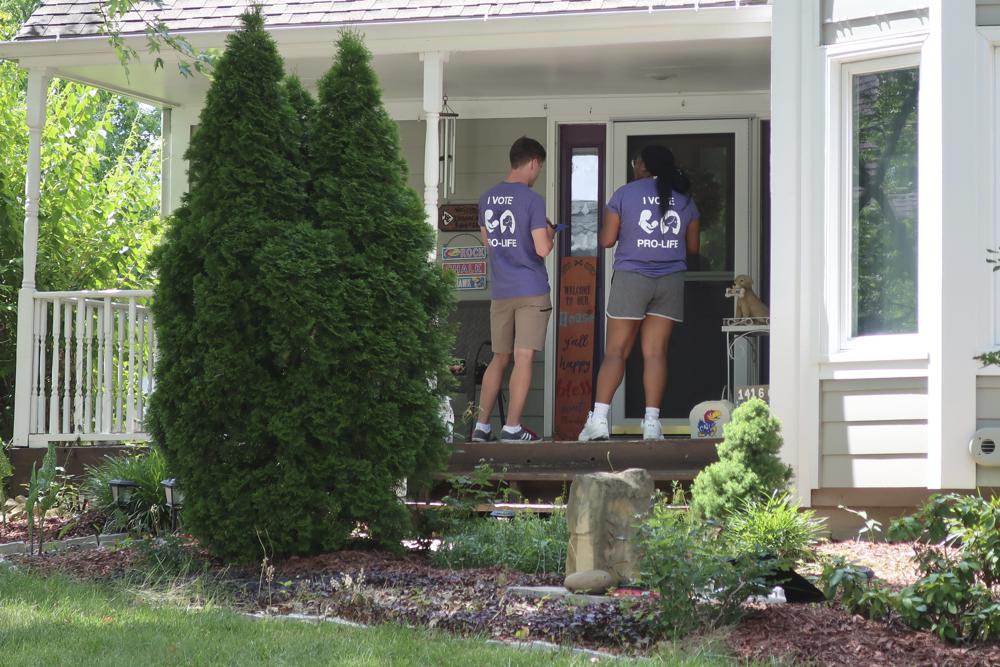 Ben Kennedy, left, and Alyssa Winters, left, wait at a door to speak with prospective voters about a proposed amendment to the Kansas Constitution that would allow legislators to further restrict or ban abortion, July 8, in Olathe, Kan.