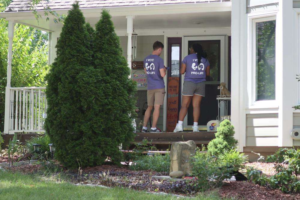Ben Kennedy, left, and Alyssa Winters, left, wait at a door to speak with prospective voters about a proposed amendment to the Kansas Constitution that would allow legislators to further restrict or ban abortion, July 8, in Olathe, Kan.
