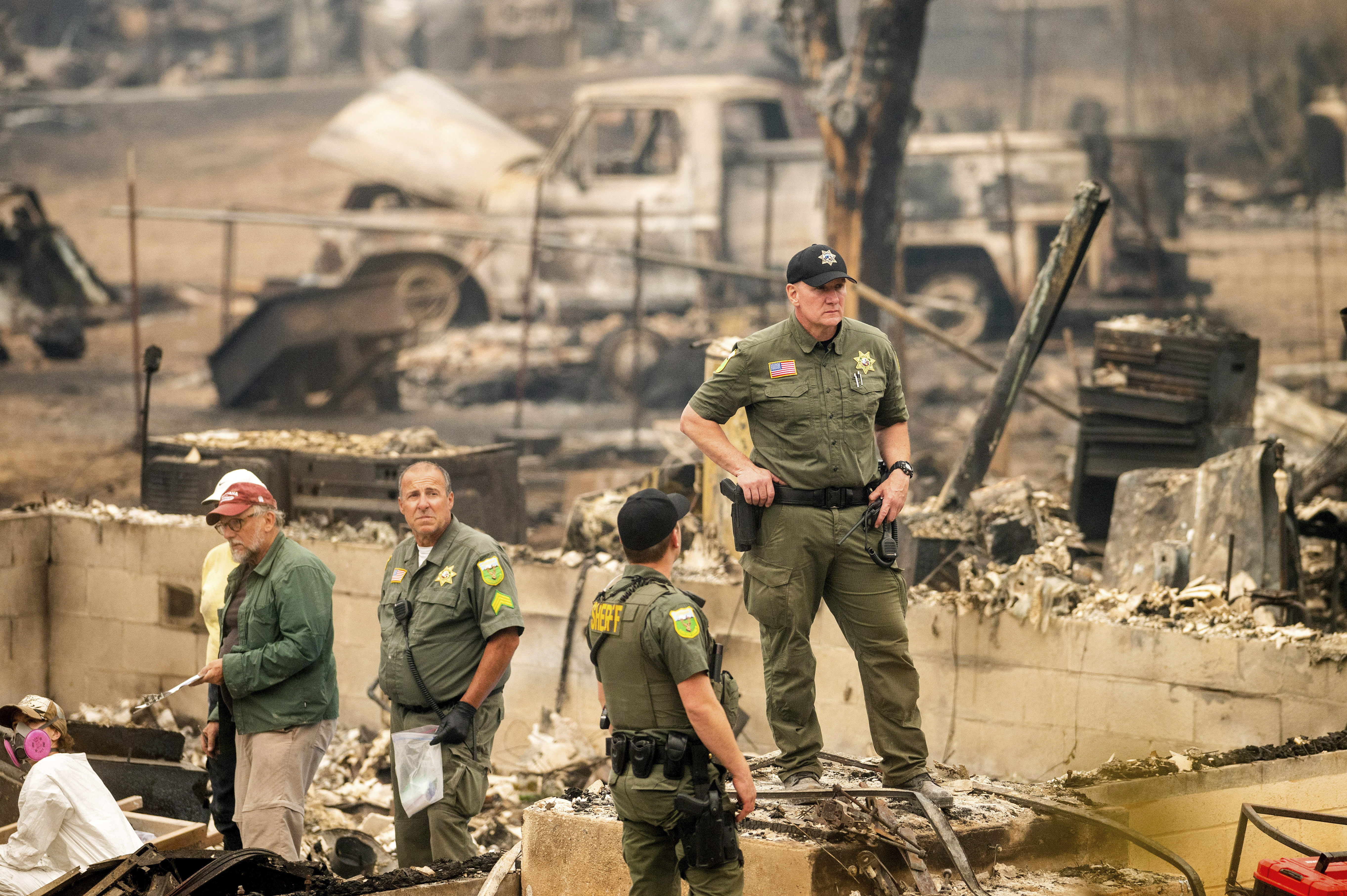 Sheriff's Deputy Johnson stands at a burned home as search and rescue workers recover the remains of a McKinney Fire victim on Monday in Klamath National Forest, Calif.