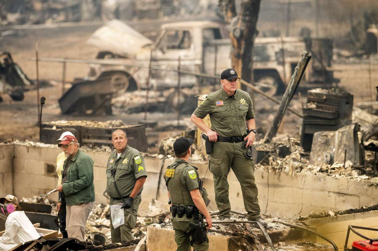 Sheriff's Deputy Johnson stands at a burned home as search and rescue workers recover the remains of a McKinney Fire victim on Monday in Klamath National Forest, Calif.