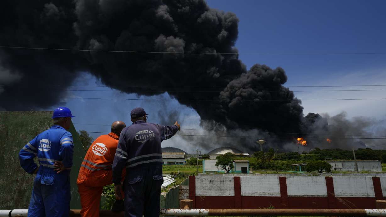 Workers of the Cuba Oil Union, known by the Spanish acronym CUPET, watch a huge rising plume of smoke from the Matanzas Supertanker Base, as firefighters work to quell a blaze that began during a thunderstorm the night before, in Matazanas, Cuba, Saturday. Cuban authorities say lightning struck a crude oil storage tank at the base, causing a fire that led to four explosions that injured more than 50 people.
