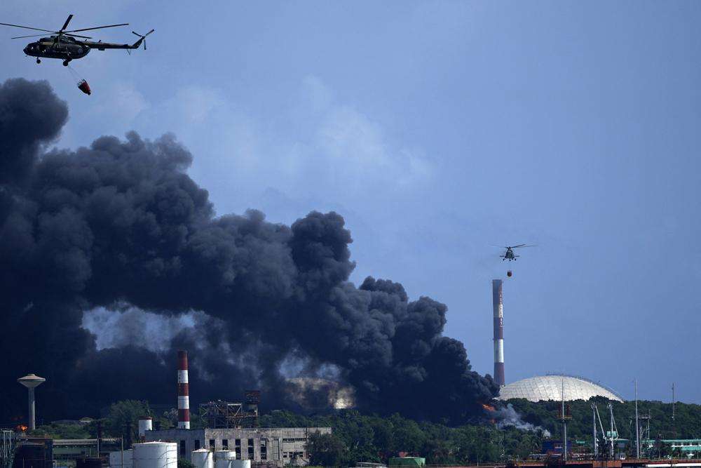 Helicopters hauling water fly over the Matanzas Supertanker Base, as firefighters and specialists work to quell the blaze which began during a thunderstorm the night before, in Matazanas, Cuba, Saturday. Cuban authorities say lightning struck a crude oil storage tank at the base, causing a fire that led to four explosions which injured more than 50 people.