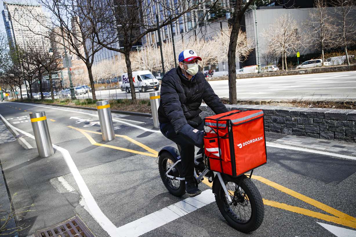 In this March 16, 2020 file photo, a delivery worker rides his bicycle along a path on the West Side Highway in New York. U.S. demand for grocery delivery is cooling as food prices rise. Some shoppers are shifting to less expensive grocery pickup, while others are returning to the store.