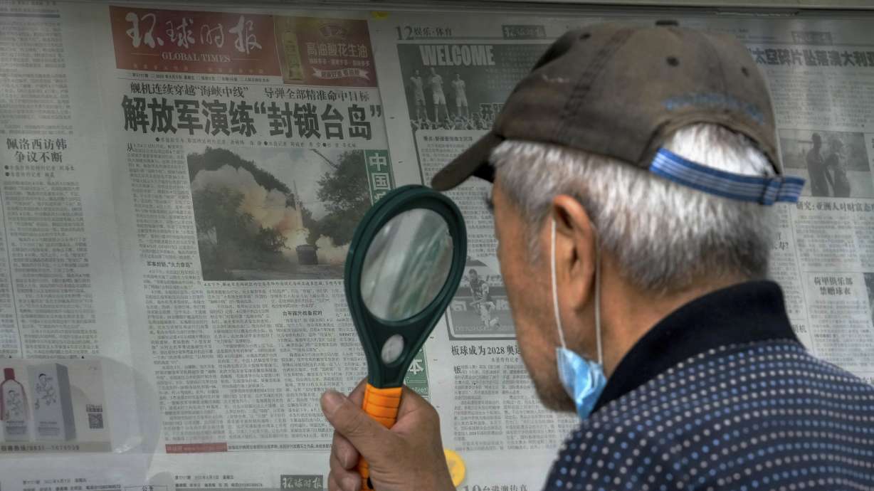 A man uses a magnifying glass to read a newspaper headline reporting on Chinese People's Liberation Army conducting military exercises, at a stand in Beijing, Sunday.
