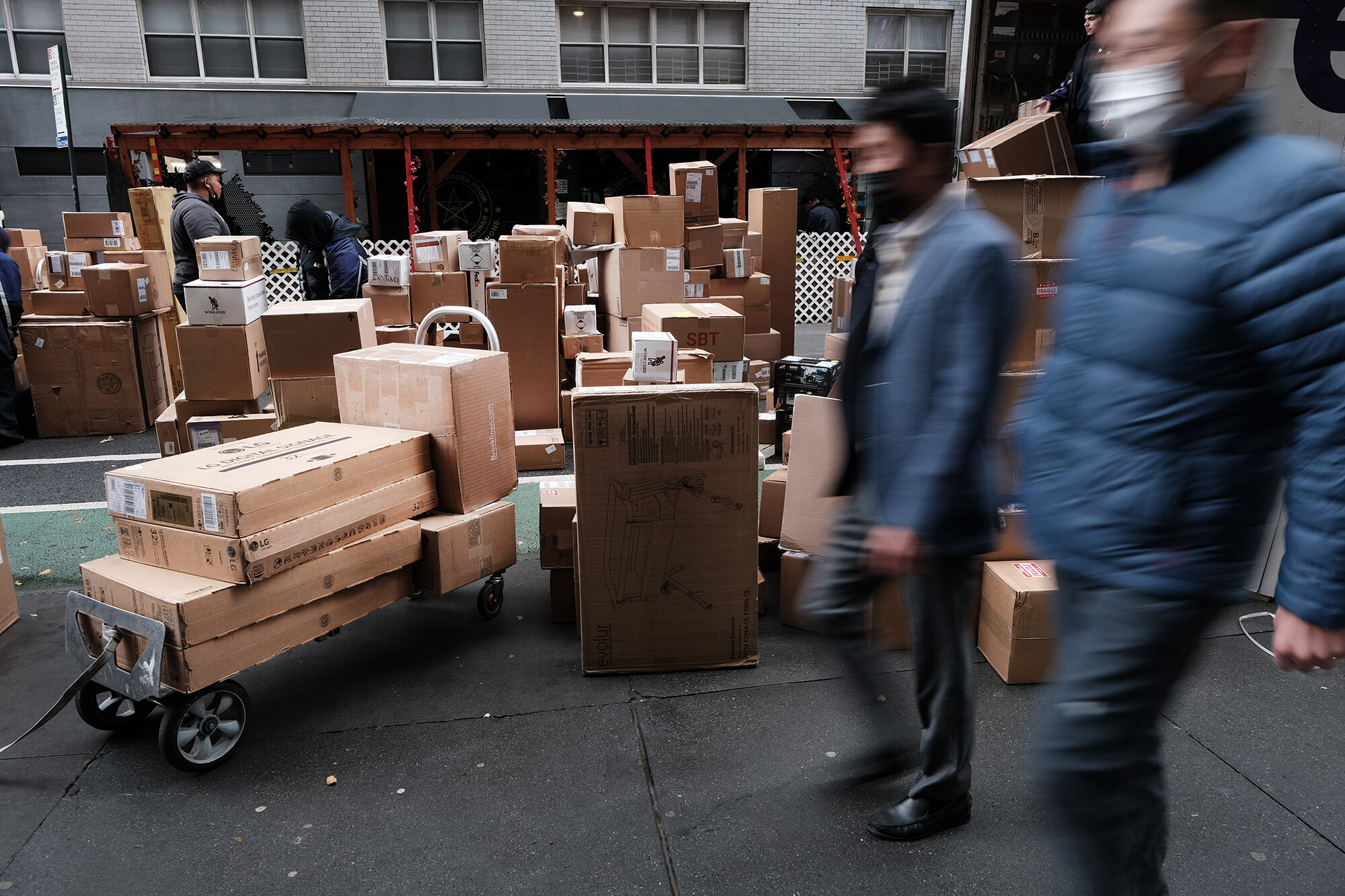 Dozens of packages are lined up along a Manhattan street as a FedEx truck makes deliveries on Dec. 6, 2021, in New York City. Online prices declined by 1% year-over-year in July, according to a report released Tuesday by Adobe.