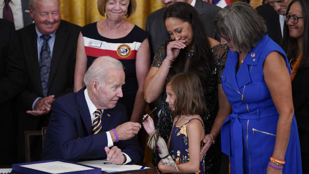 President Joe Biden gives the pen he used to sign the "PACT Act of 2022" to Brielle Robinson, daughter of Sgt. 1st Class Heath Robinson, who died of cancer two years ago, during a ceremony in the East Room of the White House, Wednesday, in Washington.