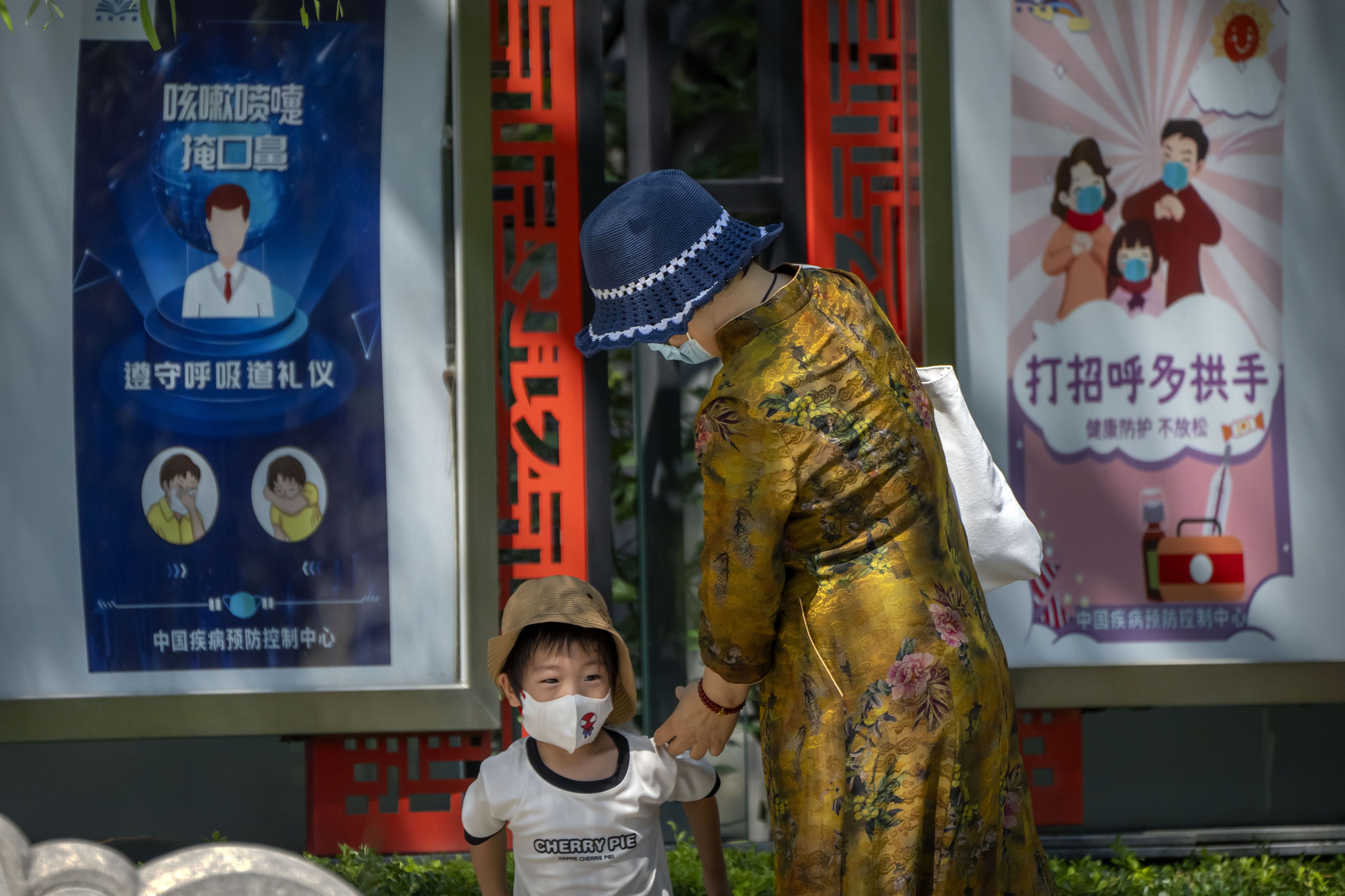 A woman and boy wearing face masks walk near posters encouraging people to wear masks and avoid handshakes at a public park in Beijing, Wednesday. Tens of thousands of travelers remain stranded on the southern Chinese resort island of Hainan but a first planeload left Tuesday.