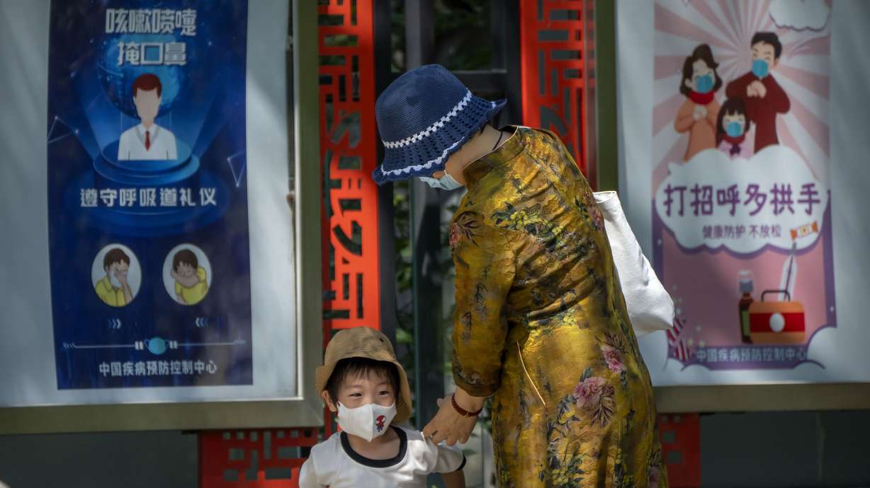 A woman and boy wearing face masks walk near posters encouraging people to wear masks and avoid handshakes at a public park in Beijing, Wednesday. Tens of thousands of travelers remain stranded on the southern Chinese resort island of Hainan but a first planeload left Tuesday.