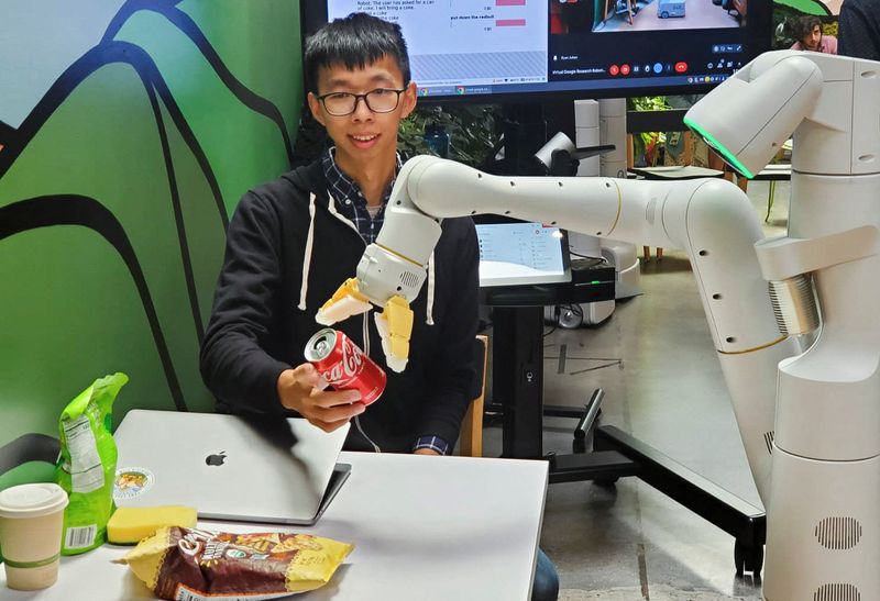 Google research scientist Fei Xia accepts a Coca-Cola can from a robot during a demonstration of AI technology at a company micro-kitchen in Mountain View, Calif., Thursday.