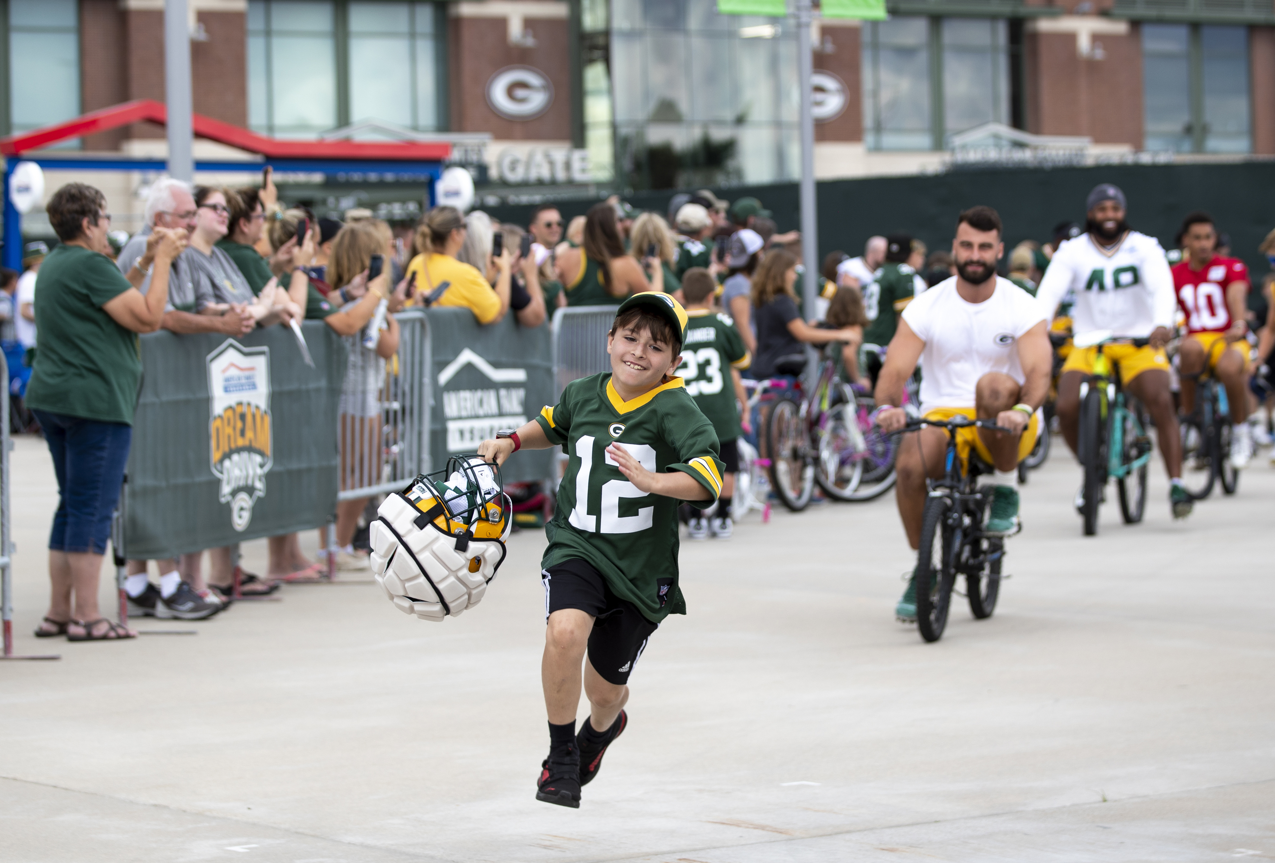 FILE - Green Bay Packers tight end Josiah Deguara, third from right, rides a young fan's bike as the fan takes off running with Deguara's helmet during the team's NFL football training camp July 27, 2022, in Green Bay, Wisc. 