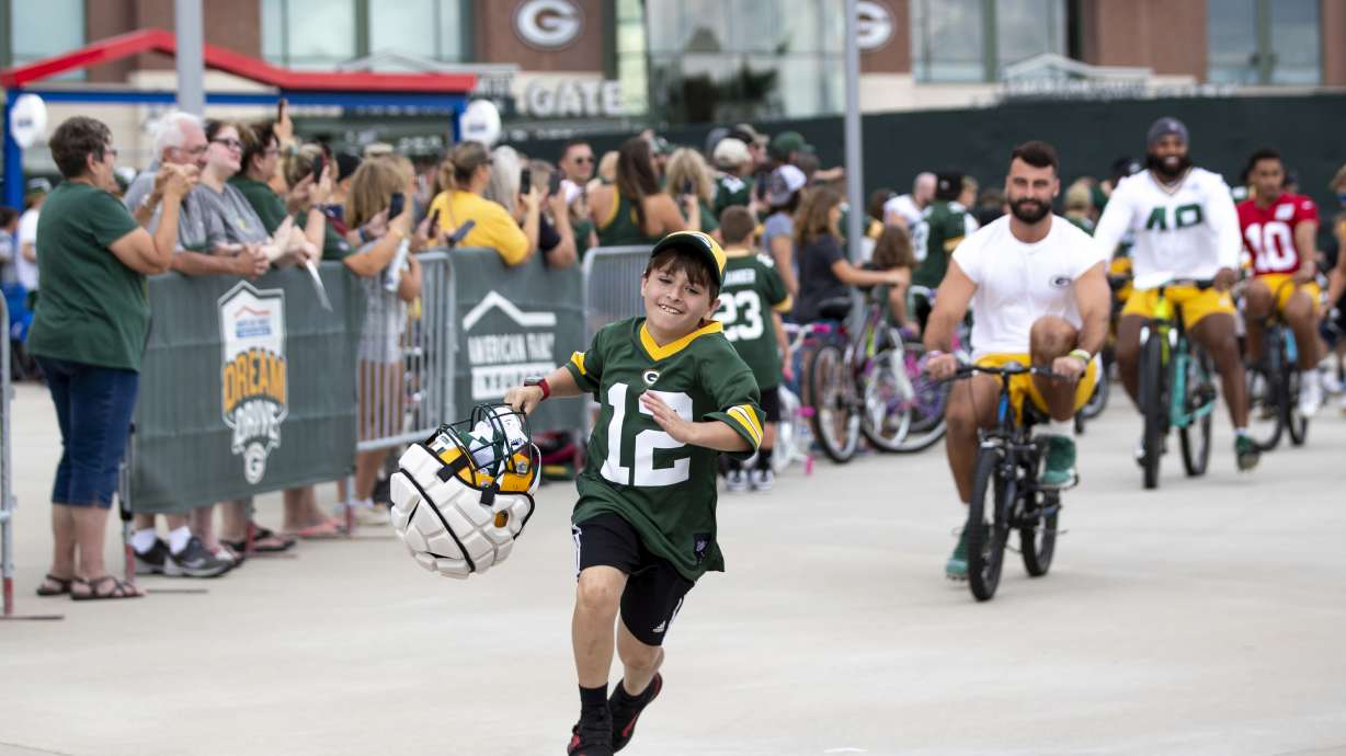 FILE - Green Bay Packers tight end Josiah Deguara, third from right, rides a young fan's bike as the fan takes off running with Deguara's helmet during the team's NFL football training camp July 27, 2022, in Green Bay, Wisc.