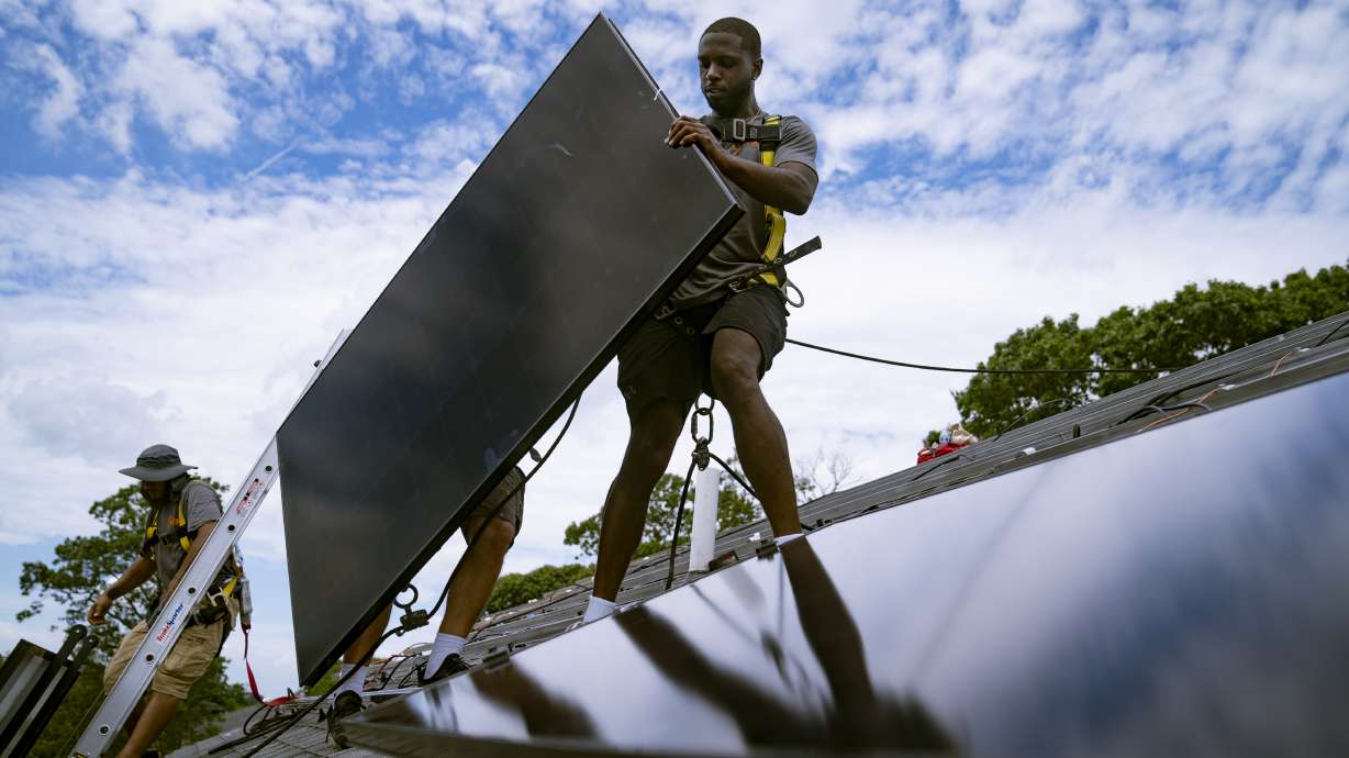 Employees of NY State Solar, a residential and commercial photovoltaic systems company, install an array of solar panels on a roof Aug. 11 in the Long Island hamlet of Massapequa, N.Y. Massive incentives for clean energy in the U.S. law signed Tuesday by President Joe Biden should reduce future global warming “not a lot, but not insignificantly either,” according to a climate scientist.
