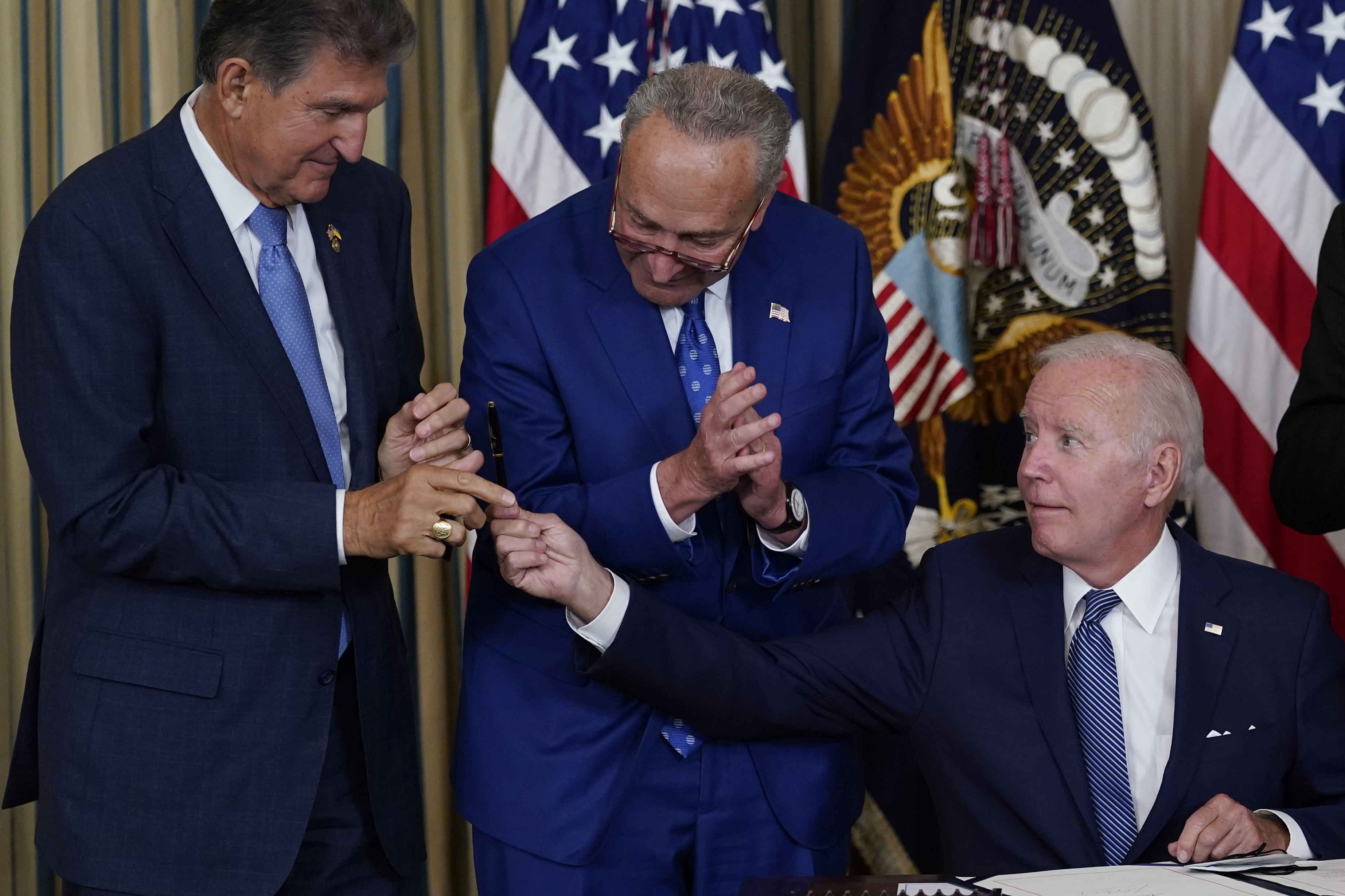 President Joe Biden hands the pen he used to sign the Democrats' landmark climate change and health care bill to Sen. Joe Manchin, D-W.Va., as Senate Majority Leader Chuck Schumer of N.Y., watches in the State Dining Room of the White House in Washington, Tuesday. The U.S. government is moving forward with its plan to award new tax credits to electric vehicle purchasers. It's part of the rollout of a huge new climate, tax and healthcare law