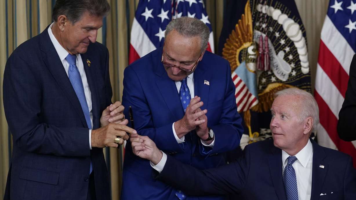 President Joe Biden hands the pen he used to sign the Democrats' landmark climate change and health care bill to Sen. Joe Manchin, D-W.Va., as Senate Majority Leader Chuck Schumer of N.Y., watches in the State Dining Room of the White House in Washington, Tuesday. The U.S. government is moving forward with its plan to award new tax credits to electric vehicle purchasers. It's part of the rollout of a huge new climate, tax and healthcare law