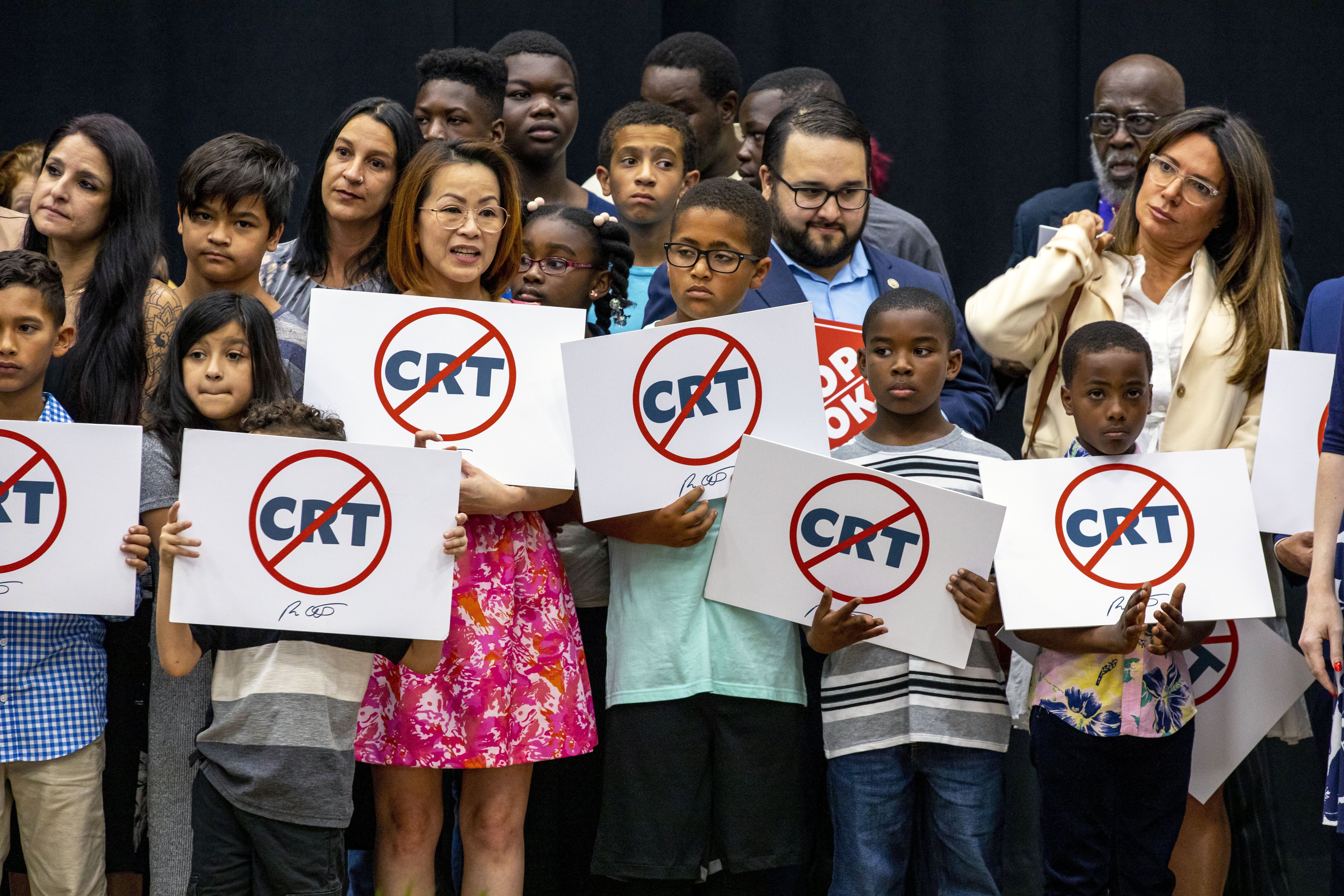 Kids holding signs against Critical Race Theory stand near Florida Gov. Ron DeSantis as he addresses the crowd before publicly signing HB7, “individual freedom,” also dubbed the “stop woke” bill in Hialeah Gardens, Fla., on April 22. A federal judge has blocked part of Florida's Stop WOKE Act.