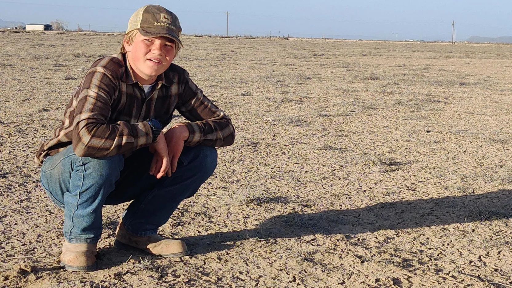 Kevin Cooper squats on dusty, fallow land near his home in Beryl, Utah.