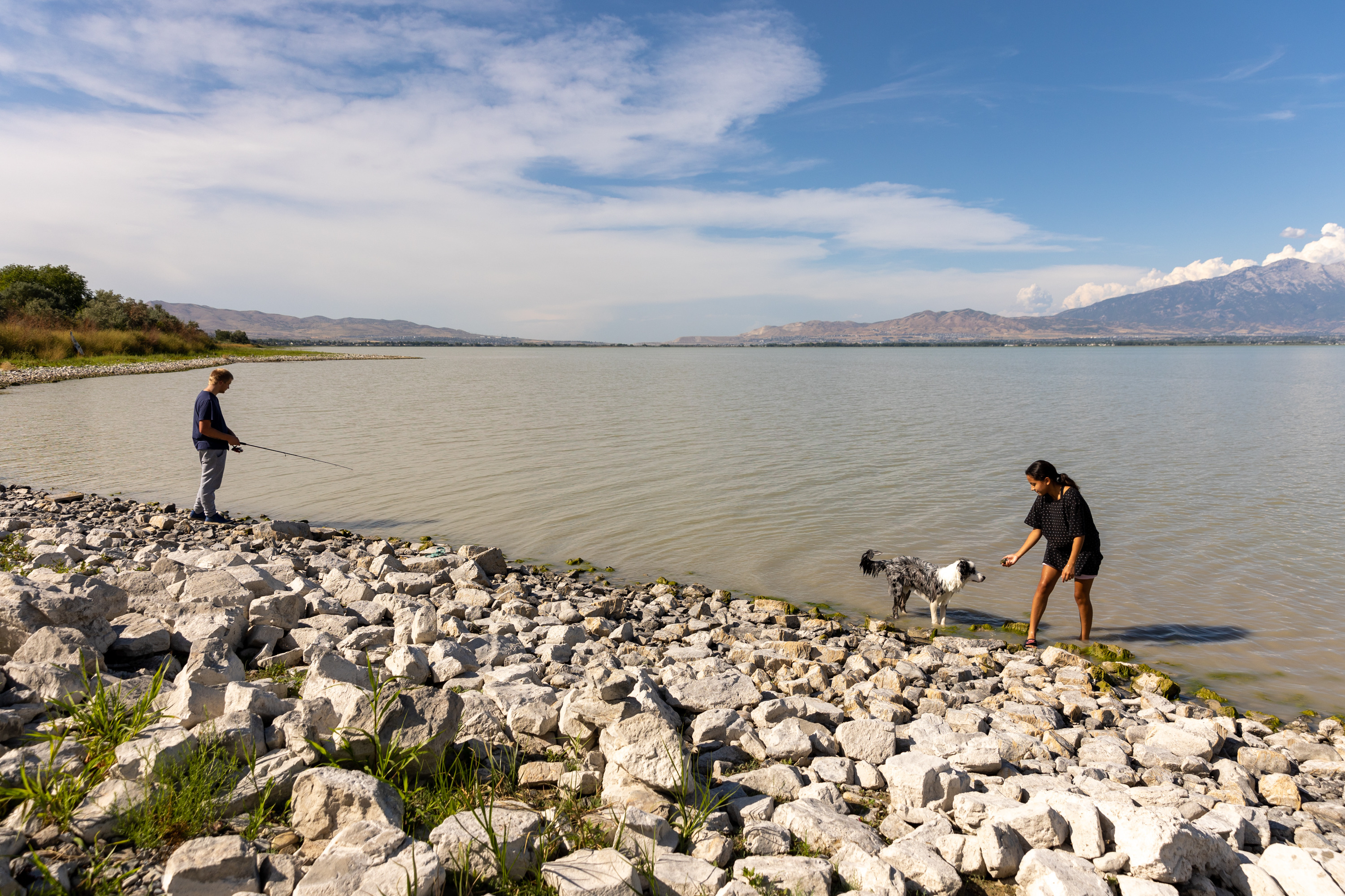Joshua Larson fishes in Utah Lake while his girlfriend, Katelyn Molen, plays with their dog, Theo, in Saratoga Springs on Aug. 22. Lake Restoration Solutions, which applied for a $6 billion plan to dredge the lake, is appealing Utah's decision to cancel the application.