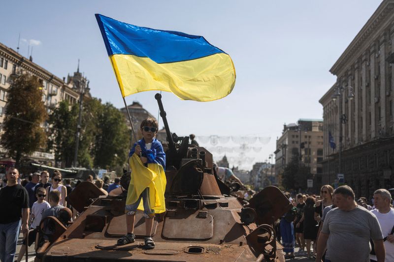 A boy waves a national flag atop of armored personal carrier at an exhibition of destroyed Russian military vehicles and weapons in Kyiv, Ukraine, Sunday. A slim majority of Americans agree that the U.S. should continue to support Kyiv until Russia withdraws all its forces.