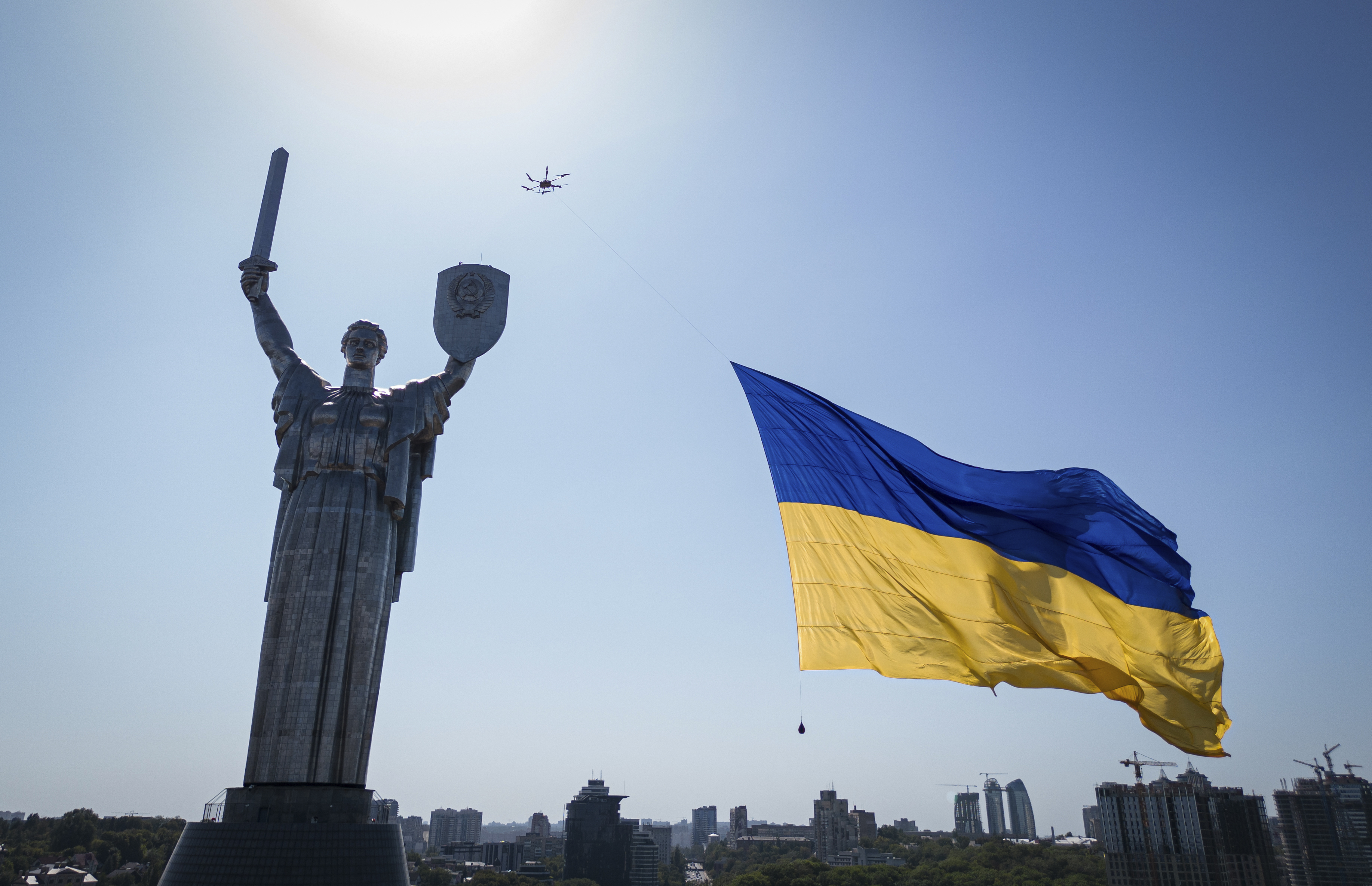 A drone carries a big national flag in front of Ukraine's the Motherland Monument in Kyiv, Ukraine, Wednesday. A Ukrainian official says the death toll from a Russian rocket attack on a train station and the surrounding area on Ukraine's Independence Day has risen to 25.