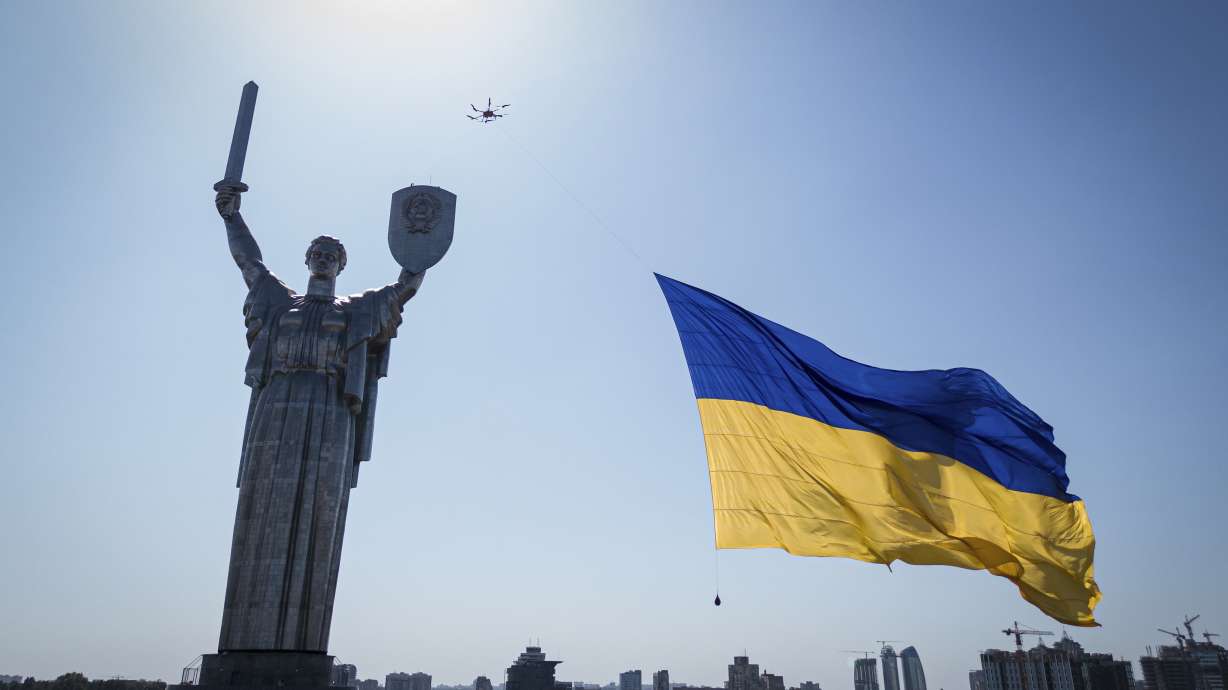 A drone carries a big national flag in front of Ukraine's the Motherland Monument in Kyiv, Ukraine, Wednesday. A Ukrainian official says the death toll from a Russian rocket attack on a train station and the surrounding area on Ukraine's Independence Day has risen to 25.