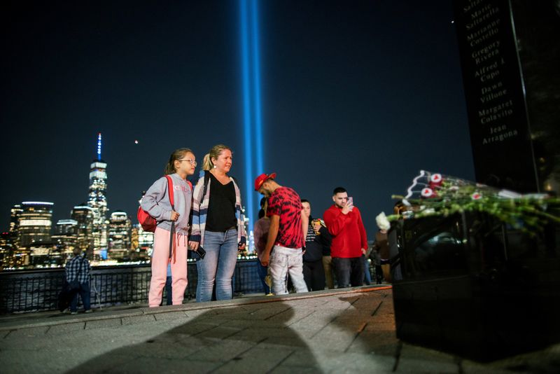 People pay respect for the victims at a memorial while the Tribute in Light art installation and the One World Trade Center are seen in the background on the 20th anniversary of the Sept. 11, 2001, attacks in New York City, as it is seen from Exchange Place, New Jersey, Sept. 11, 2021.