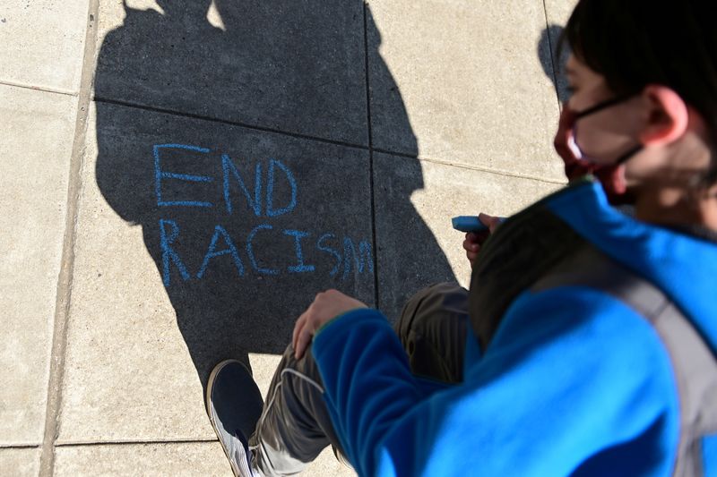 A child writes, "End racism" in chalk on a sidewalk as people rally to protest recent violence against people of Asian descent, in Washington, March 21, 2021. A UN committee on Tuesday condemned the overturning of the constitutional right to abortion in the United States, saying it was hitting racial and ethnic minorities hardest and asked Washington to take mitigation measures.