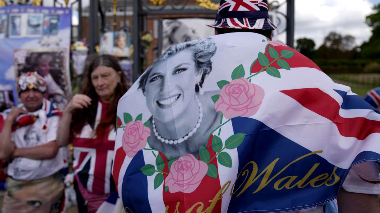 People wave a flag as they stand in front of messages of remembrance for Princess Diana outside the gates of Kensington Palace, in London, Wednesday. Wednesday marks the 25th anniversary of Princess Diana's death in a Paris car crash.