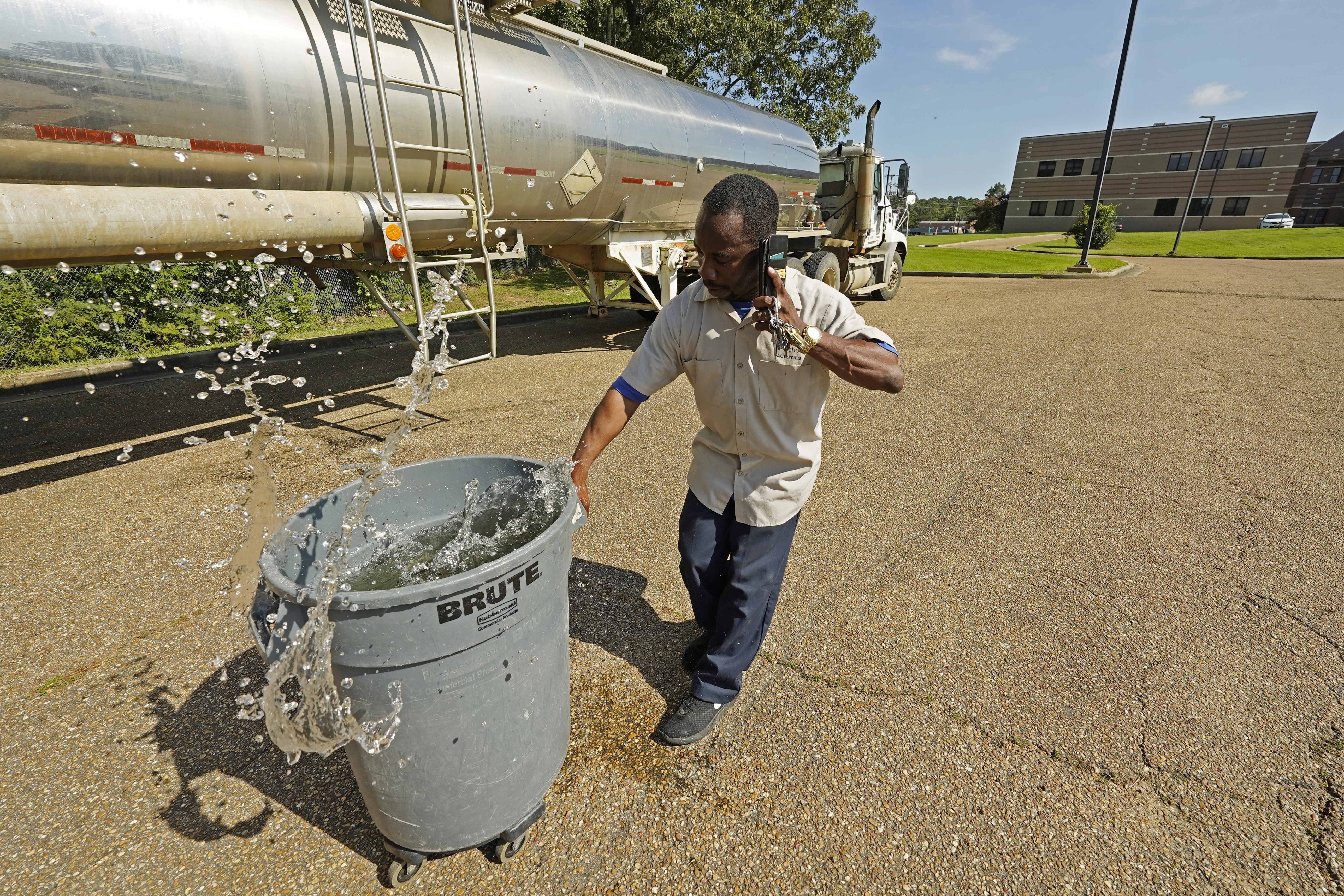 Santonia Matthews, a custodian at Forest Hill High School in Jackson, Miss., hauls away a trash can filled with water from a tanker in the school's parking lot, Wednesday, Aug. 31, 2022. The tanker is one of two placed strategically in the city to provide residents non-potable water. The recent flood worsened Jackson's longstanding water system problems and the state Health Department has had Mississippi's capital city under a boil-water notice since late July. 