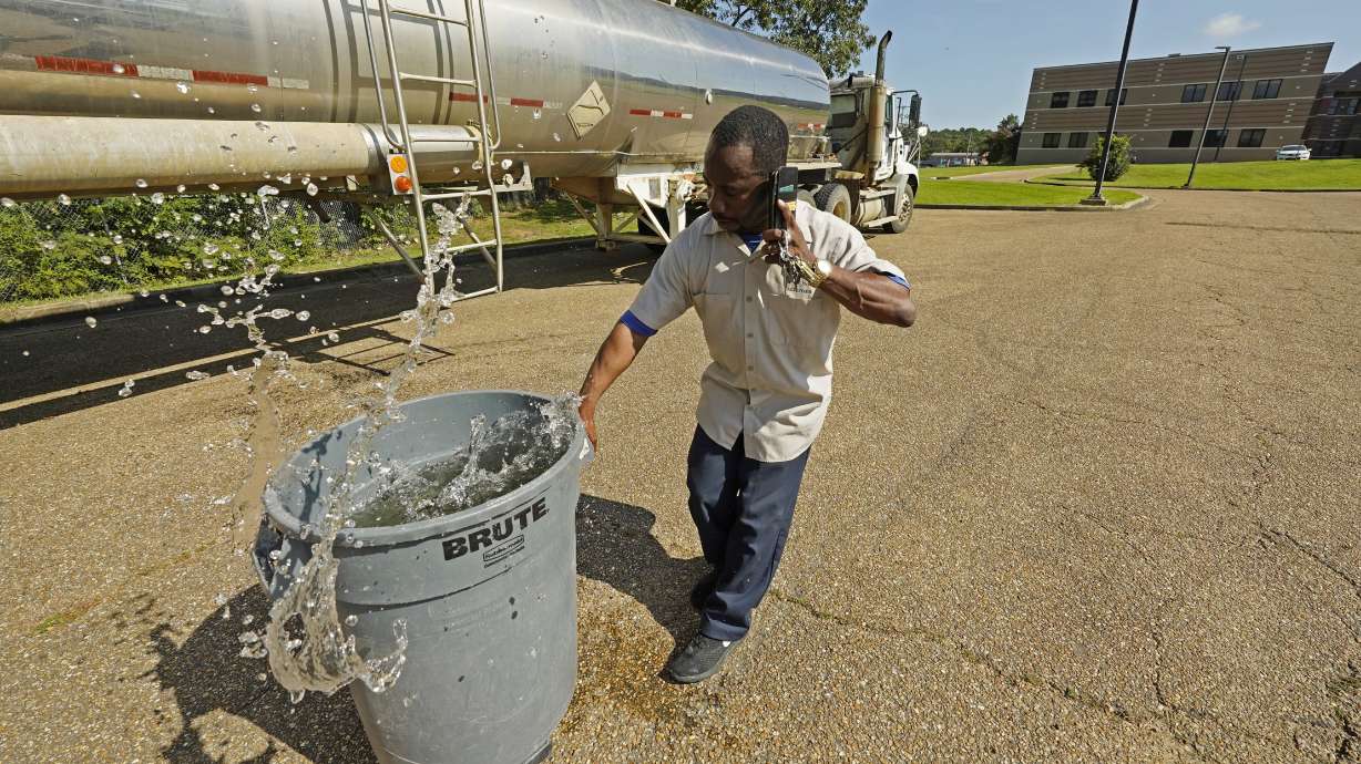 Santonia Matthews, a custodian at Forest Hill High School in Jackson, Miss., hauls away a trash can filled with water from a tanker in the school's parking lot, Wednesday, Aug. 31, 2022. The tanker is one of two placed strategically in the city to provide residents non-potable water. The recent flood worsened Jackson's longstanding water system problems and the state Health Department has had Mississippi's capital city under a boil-water notice since late July.