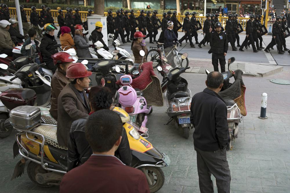 Residents watch a convoy of security personnel armed with batons and shields patrol through central Kashgar in western China's Xinjiang region, Nov. 5, 2017. China's discriminatory detention of Uyghurs and other mostly Muslim ethnic groups in the western region of Xinjiang may constitute crimes against humanity, the U.N. human rights office said in a long-awaited report Wednesday, which cited "serious" rights violations and patterns of torture in recent years. 