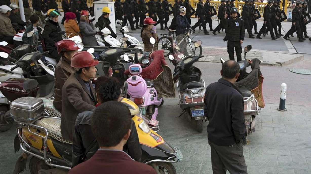 Residents watch a convoy of security personnel armed with batons and shields patrol through central Kashgar in western China's Xinjiang region, Nov. 5, 2017. China's discriminatory detention of Uyghurs and other mostly Muslim ethnic groups in the western region of Xinjiang may constitute crimes against humanity, the U.N. human rights office said in a long-awaited report Wednesday, which cited "serious" rights violations and patterns of torture in recent years.