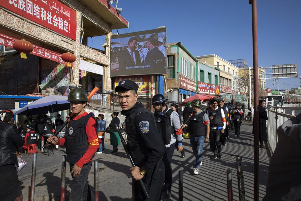 Armed civilians patrol the area outside the Hotan Bazaar where a screen shows Chinese President Xi Jinping in Hotan in western China's Xinjiang region, Nov. 3, 2017. China's discriminatory detention of Uyghurs and other mostly Muslim ethnic groups in the western region of Xinjiang may constitute crimes against humanity, the U.N. human rights office said in a long-awaited report Wednesday which cited "serious" rights violations and patterns of torture in recent years.