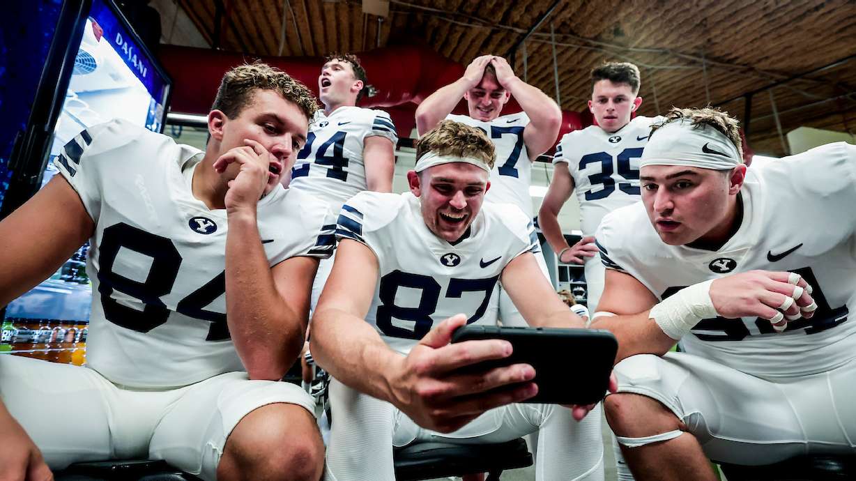 BYU players watch college football games on a cell phone during a weather delay before the Cougars' season opener at South Florida, Saturday, Sept. 3, 2022 in Tampa, Fla.