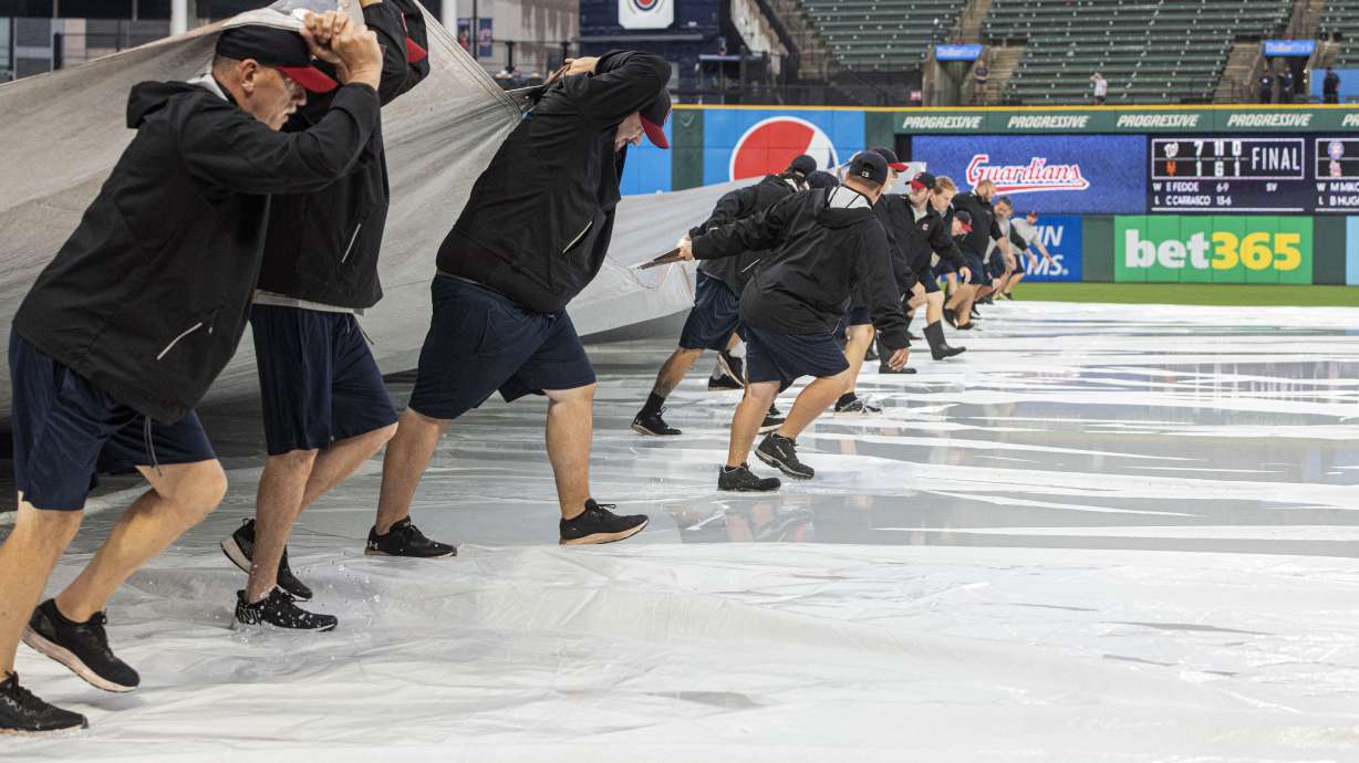 Members of the Cleveland Guardians grounds crew remove the tarp from the infield as they attempt to get the field ready to play during the fourth inning of a baseball game between the Seattle Mariners and the Guardians in Cleveland, Sunday, Sept. 4, 2022.