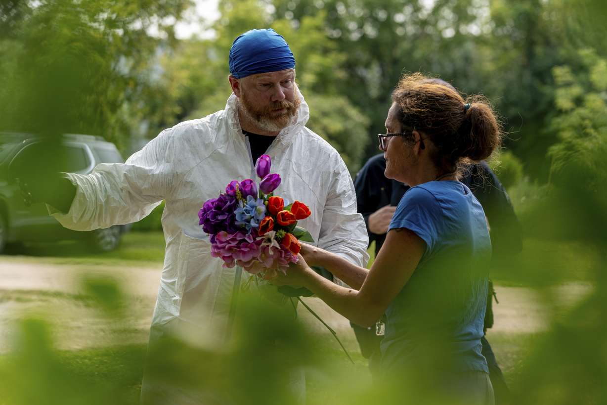 Ruby Works speaks with a forensic investigator before bringing flowers to the home of a victim who has been identified by residents as Wes Petterson in Weldon, Saskatchewan, on Monday. Works said that the 77-years-old victim was like an uncle to her.