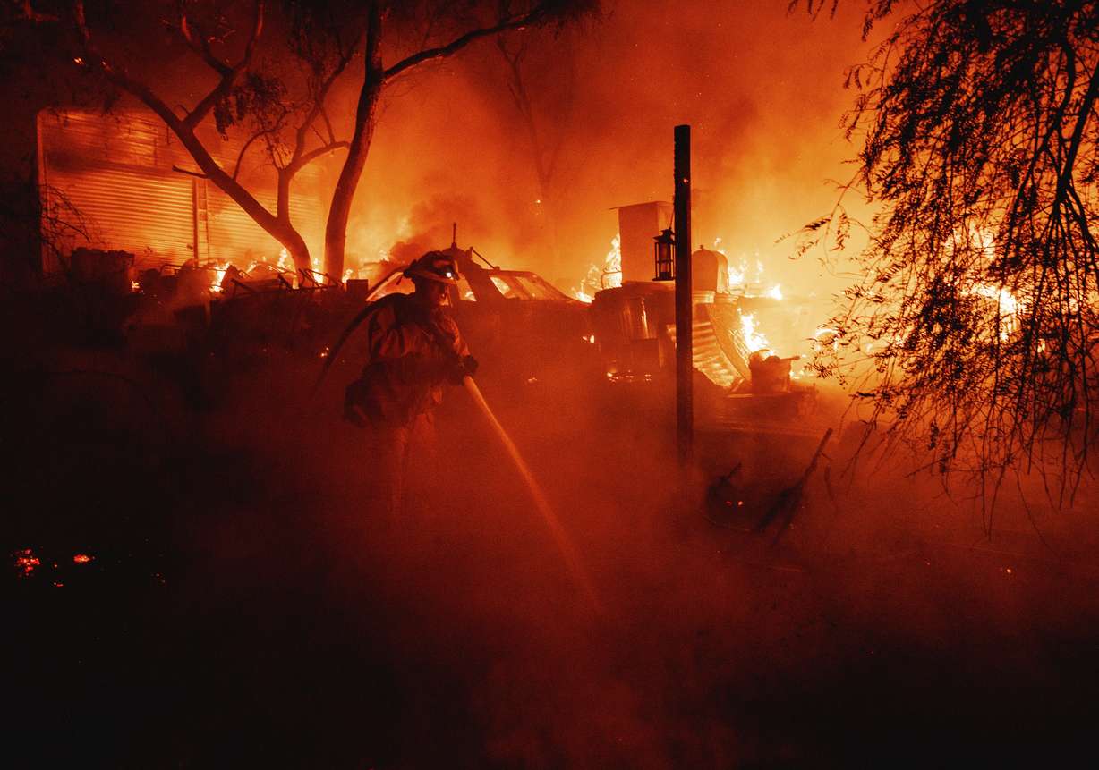 A firefighter takes a hose to a burning property while battling the Fairview Fire Monday near Hemet, Calif.