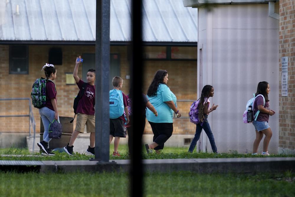 Students are escorted at Uvalde Elementary, now protected by a fence and Texas State Troopers, for the first day of school, Tuesday, in Uvalde. Students in Uvalde are returning to campuses for the first time since the shootings at Robb Elementary where two teachers and 19 students were killed.