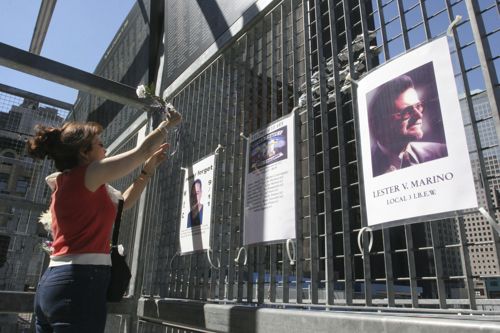 Kathy Haberman places a flower and card in memory of her daughter Andrea Haberman on a gate with other memorial images surrounding ground zero in New York, Sept. 10, 2005. Nearly two decades after his capture in Pakistan, the self-described mastermind of the Sept. 11 terror attacks is still in a legal limbo. 