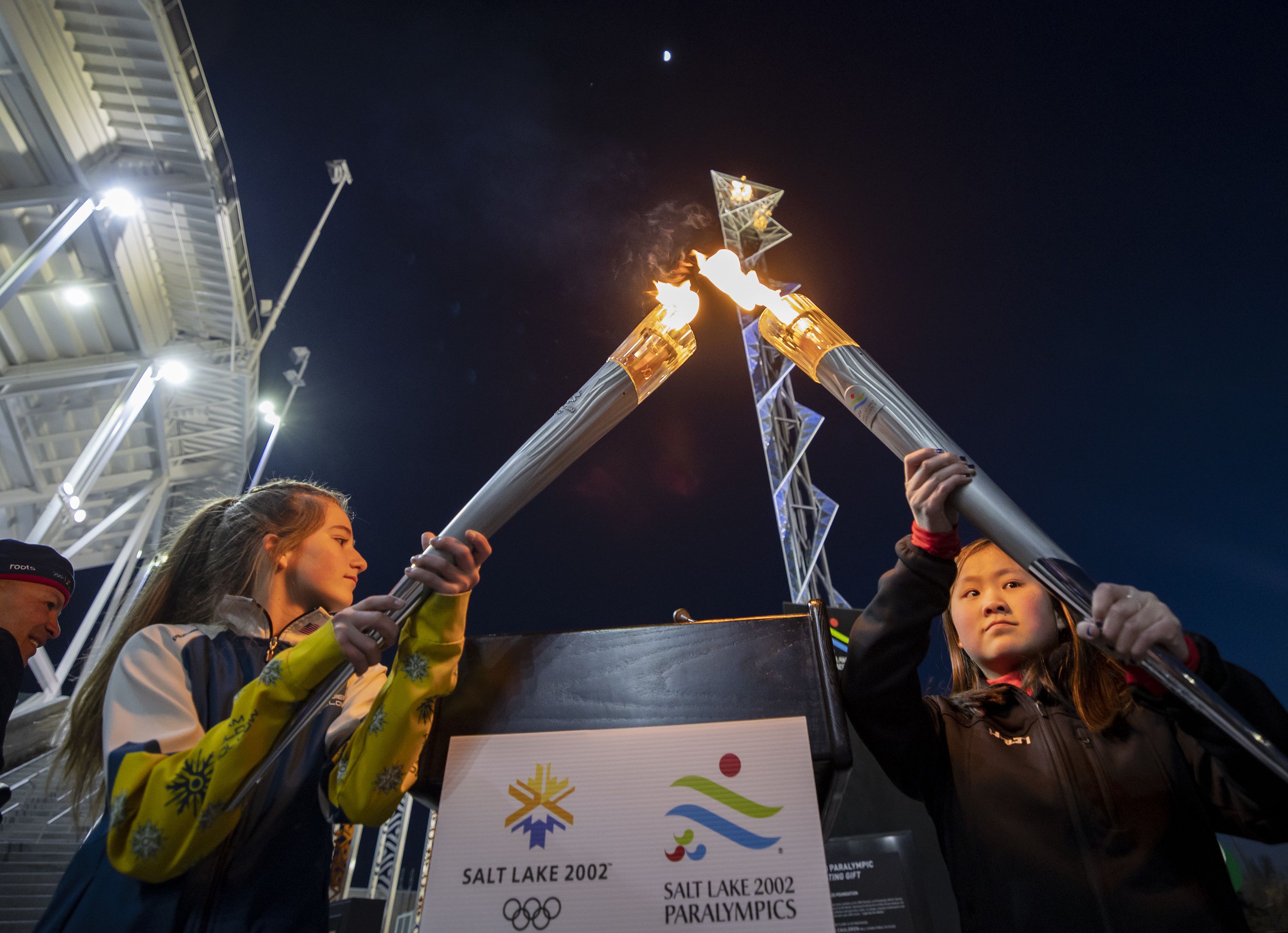 Gabrielle Harris and YiYi O’Brien combine Olympic torches from 2002 as the flame at Rice-Eccles Stadium in Salt Lake City is lit on Feb. 8, marking the 20th anniversary of the 2002 Olympic Games in Salt Lake City. It may take a while for the International Olympic Committee was expected to settle on a host city for the 2030 Winter Games.