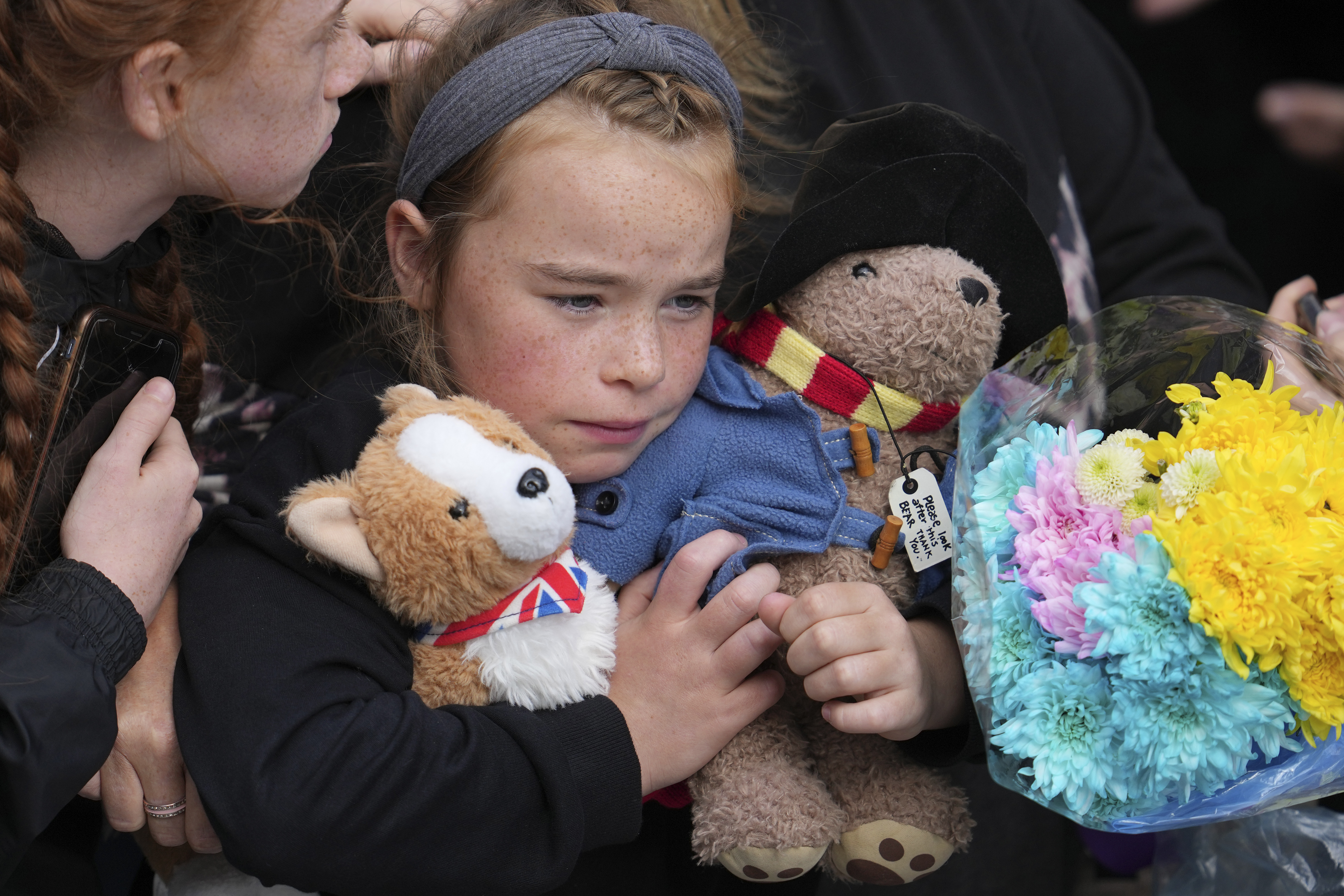 A young girl holds a Paddington bear and a Corgi dog stuffed toys while waiting to watch the Procession of Queen Elizabeth's coffin from the Palace of Holyroodhouse to St Giles Cathedral on the Royal Mile in Edinburgh, Scotland, Monday.