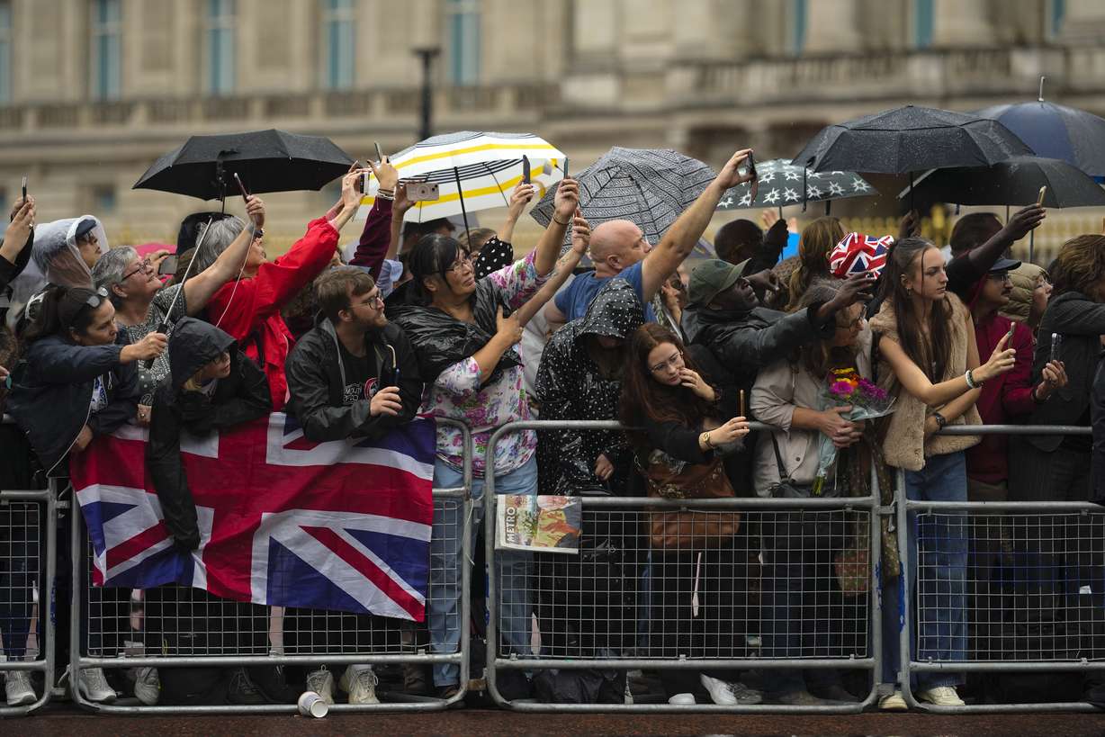 People wait for the arrival of the hearse carrying Queen Elizabeth's coffin at Buckingham Palace in London, Tuesday.