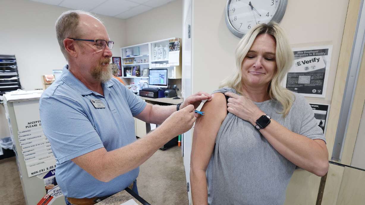 Pharmacist Tad Jolley vaccinates gift shop employee Kamie White with a flu shot at Jolley’s Pharmacy in West Jordan on Tuesday. Flu shots aren't something most people think about until later in the fall or even winter. But that's changing this year now that everyone is being urged to get the newly updated COVID-19 booster shots as soon as they're eligible.