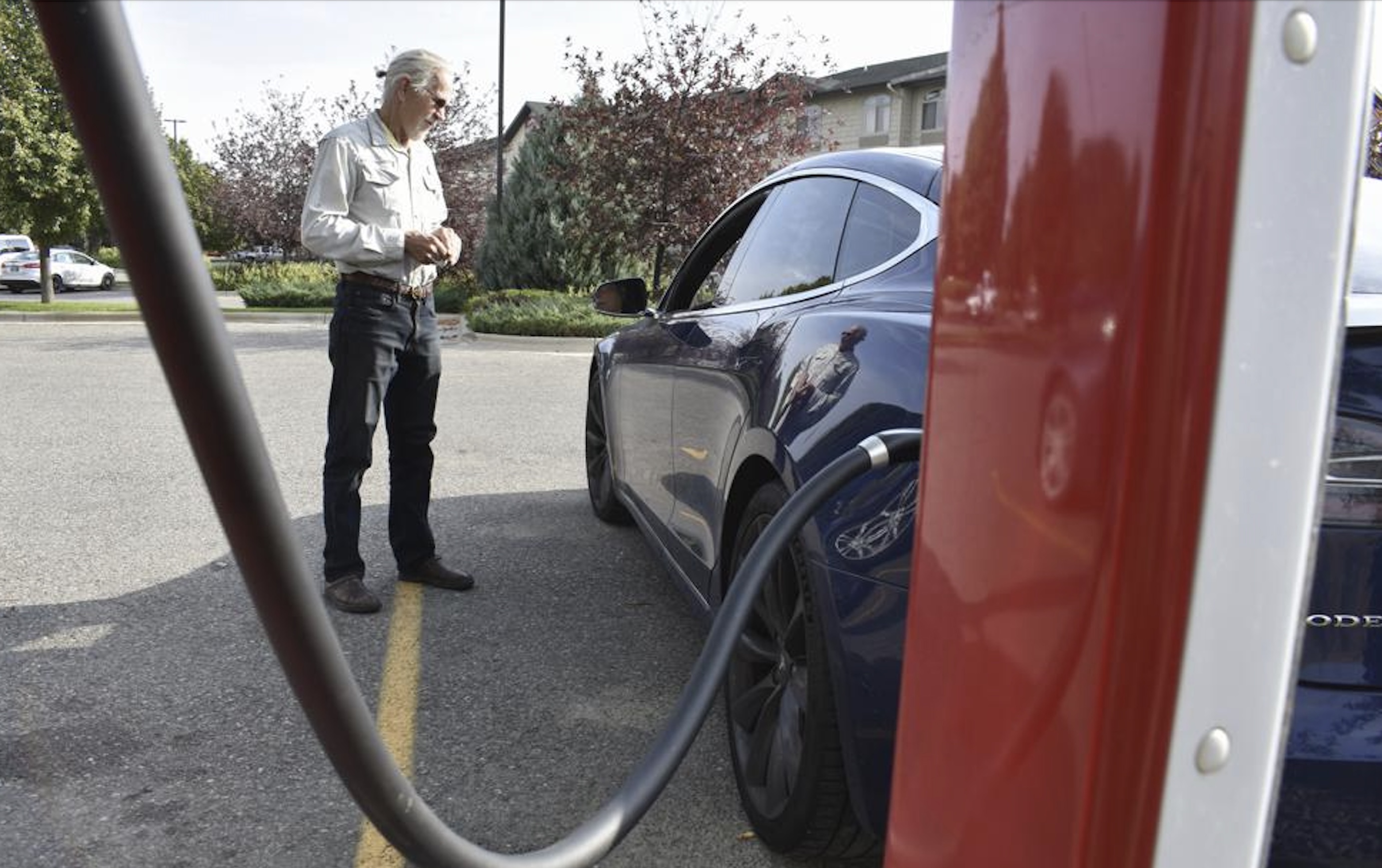 Bob Palrud of Spokane, Wash. speaks with a fellow electric vehicle owner who is charging up at a station along Interstate 90, on Wednesday in Billings, Mont. Palrud says distances between EV charging stations are always on his mind during lengthy journeys across the U.S. West where such infrastructure remains sparse.
