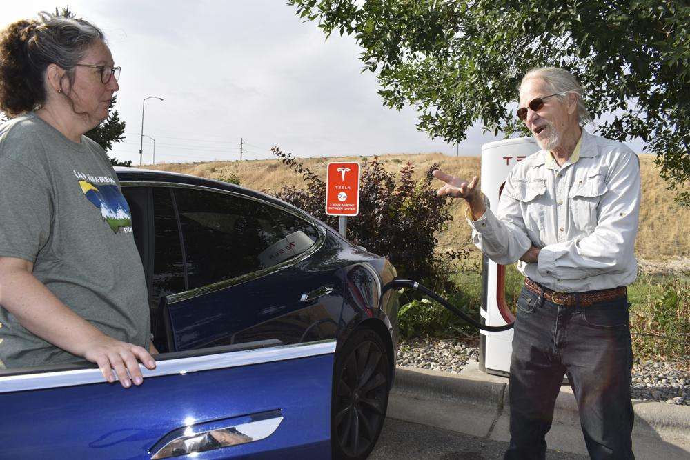Jeannette Englehart of Billings, Mont. (left) stands outside her car speaking with fellow electric vehicle owner Bob Palrud of Spokane, Wash. at a charging station near Interstate 90, on Wednesday in Billings, Mont. Officials from rural states in the U.S. west are pushing the Biden administration to ease requirements for charging stations because of limited demand in areas with low population densities.